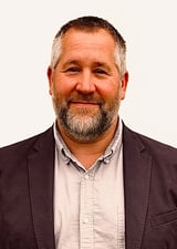 Headshot of a middle-aged man with gray beard wearing a dark blazer
